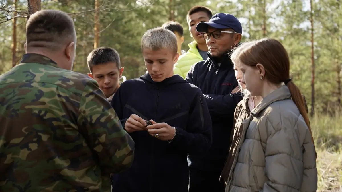 Воспитание природой: в «Семей орманы» организовали экологическую экскурсию для детей Слайд 1 из 7. Человек в камуфляже что-то показывает группе подростков и мужчине в лесу.